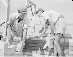 Black and white photo: men building a brick wall.