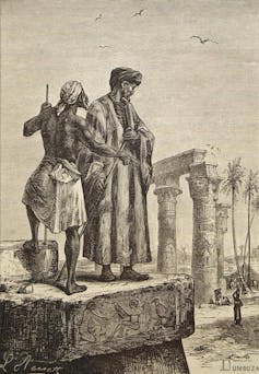 A man in a long robe beside ancient Roman columns.