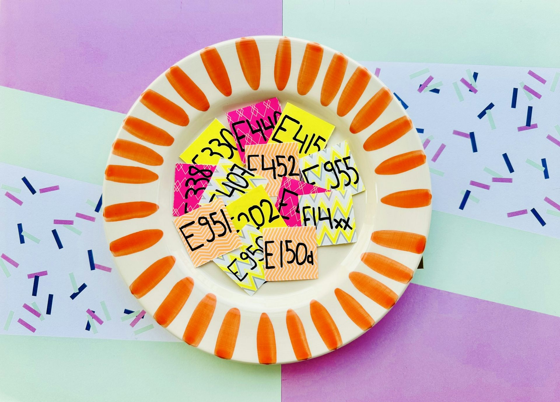 Une assiette colorée est remplie de vignettes avec les noms de codes d’additifs alimentaires.