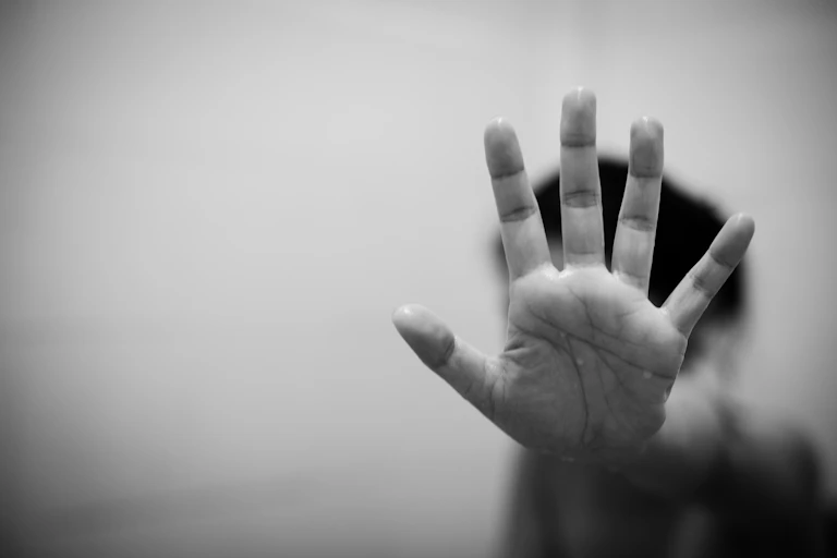 black and white photo of a young person sticking their hand out towards the camera in a 'stop' gesture