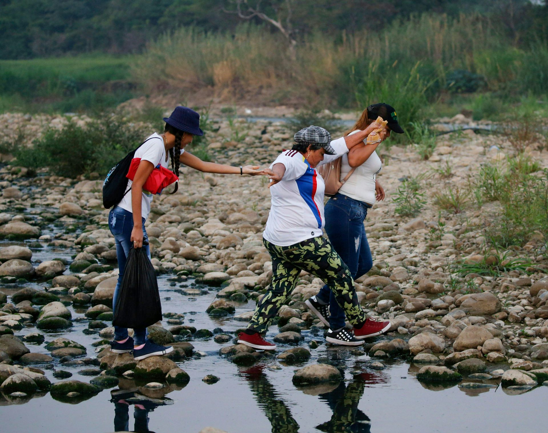Three women walk across the Tachira river between Venezuela and Colombia.