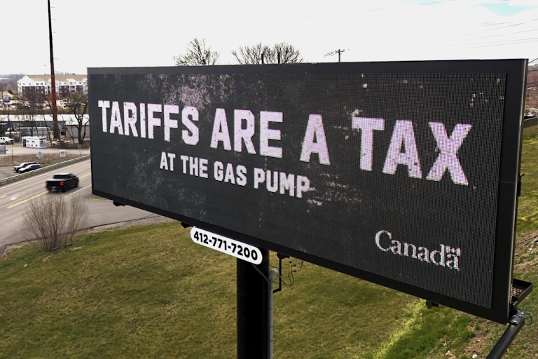 An electronic billboard reads Tariffs are a Tax at The Gas Pumps with a Canada insignia on the bottom right.