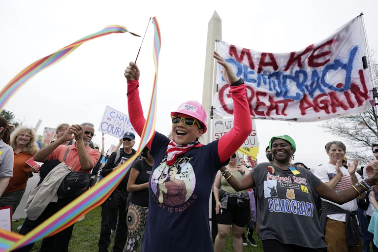 People at a protest smile and wave signs and ribbons.