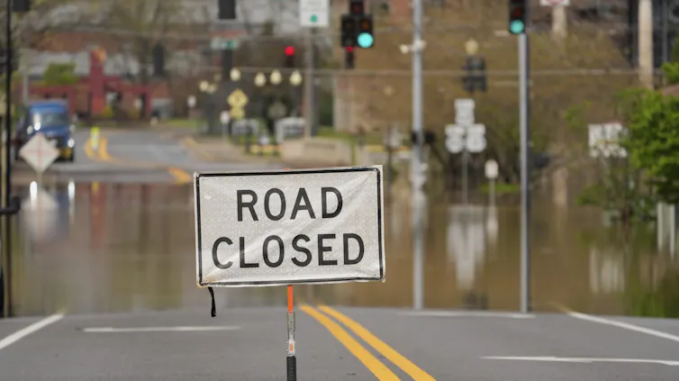 A flooded street with a 'road closed' sign and brick buildings in the background.