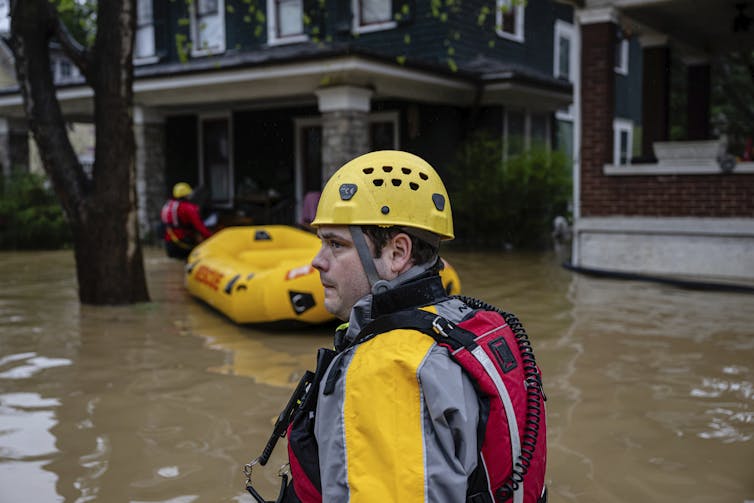 Rescuers with an inflated boat walk in waist-deep water toward older brick houses.