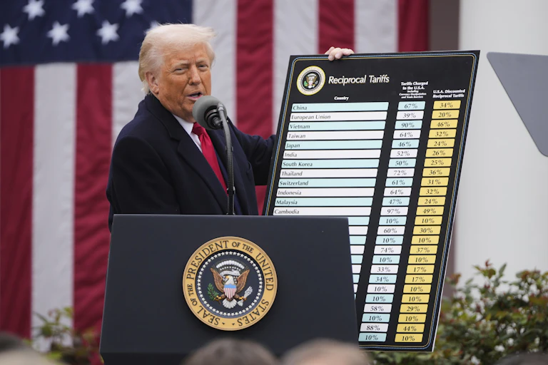 A white man in a suit with orange-tinged skin and white hair holds up a giant chart that says 'Reciprocal tariffs' at the top