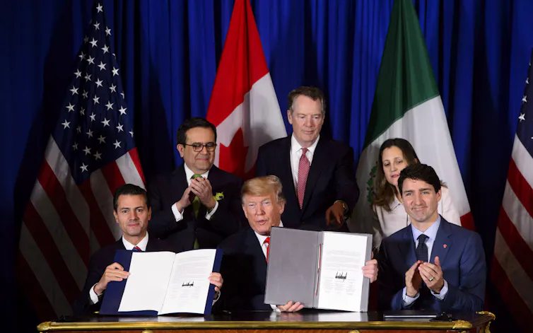 A Mexican man and a white man each hold up a signed document while a second white man claps beside them