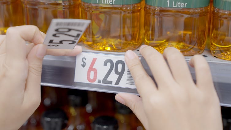 A pair of hands swapping a 5.29 price tag on a shelf for a 6.29 price tag