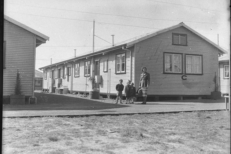 Black and white photograph, a family in front of a long one story builidng