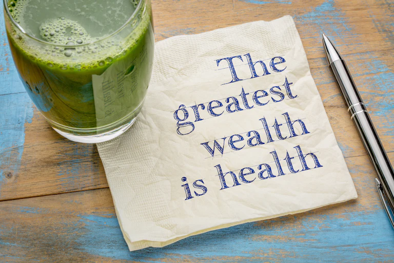 A glass of green juice sitting on a napkin that reads 'The greatest wealth is health.'