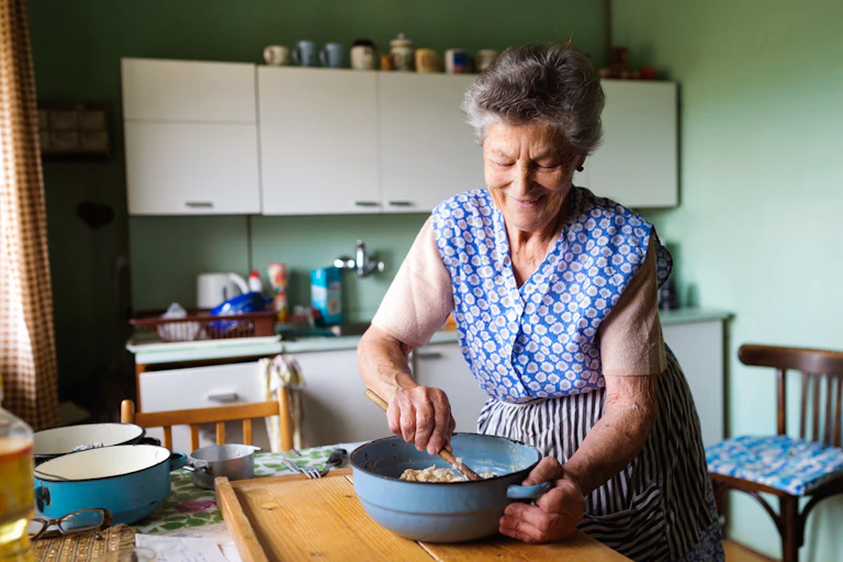 Elderly woman cooking in her kitchen, mixing ingredients in cast iron pot