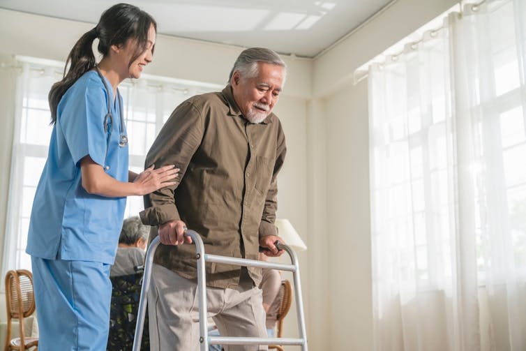 Health worker helping elderly man with walking frame