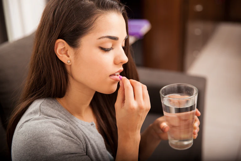 A young woman holds a pink pill in front of her lips.
