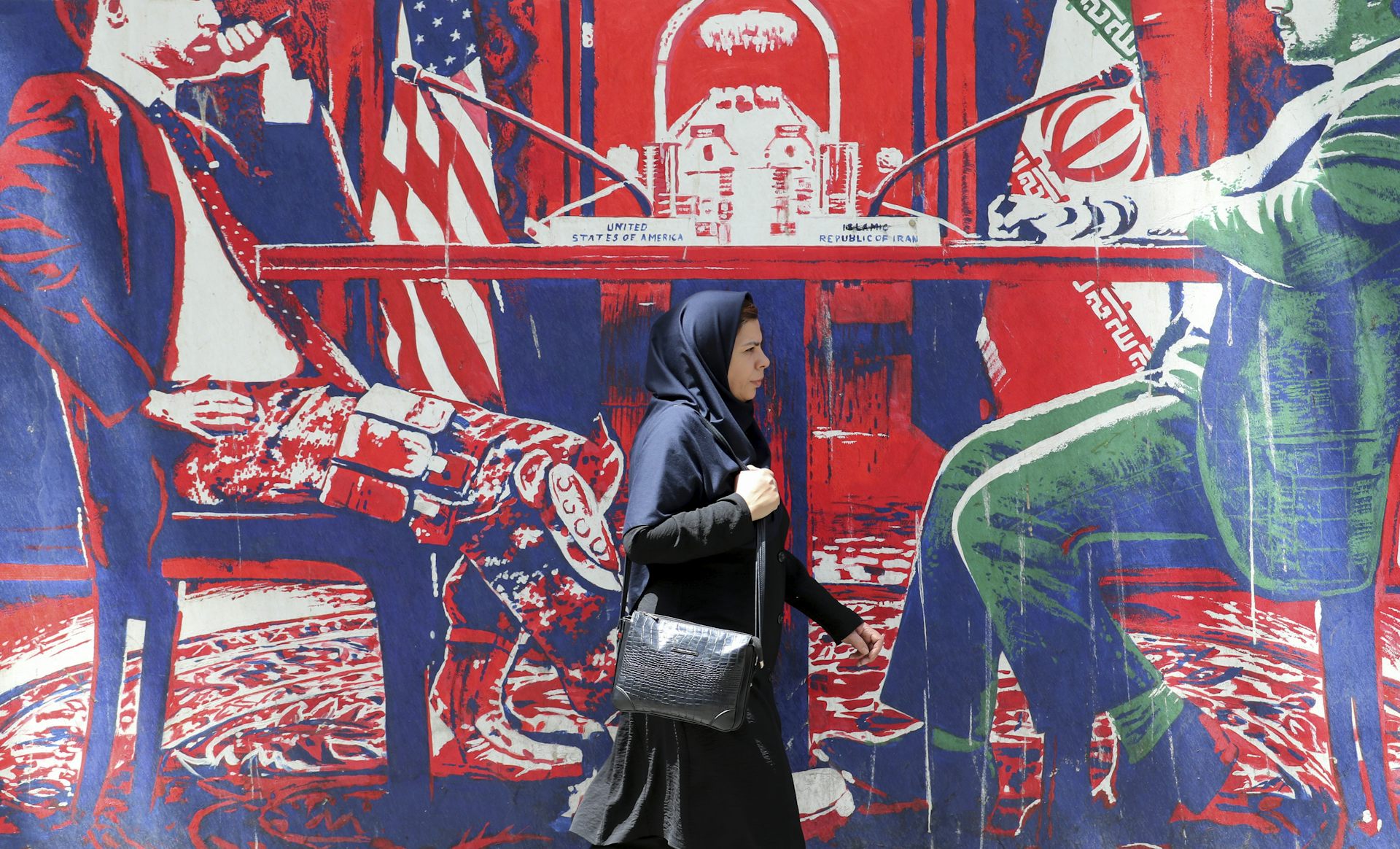 A woman walks outside the former US embassy in Tehran which is decorated with murals showing US and Iran in negotiations.