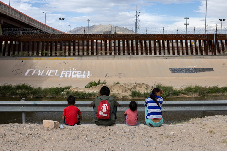 Un grupo de niños ante una valla observa el otro lado.