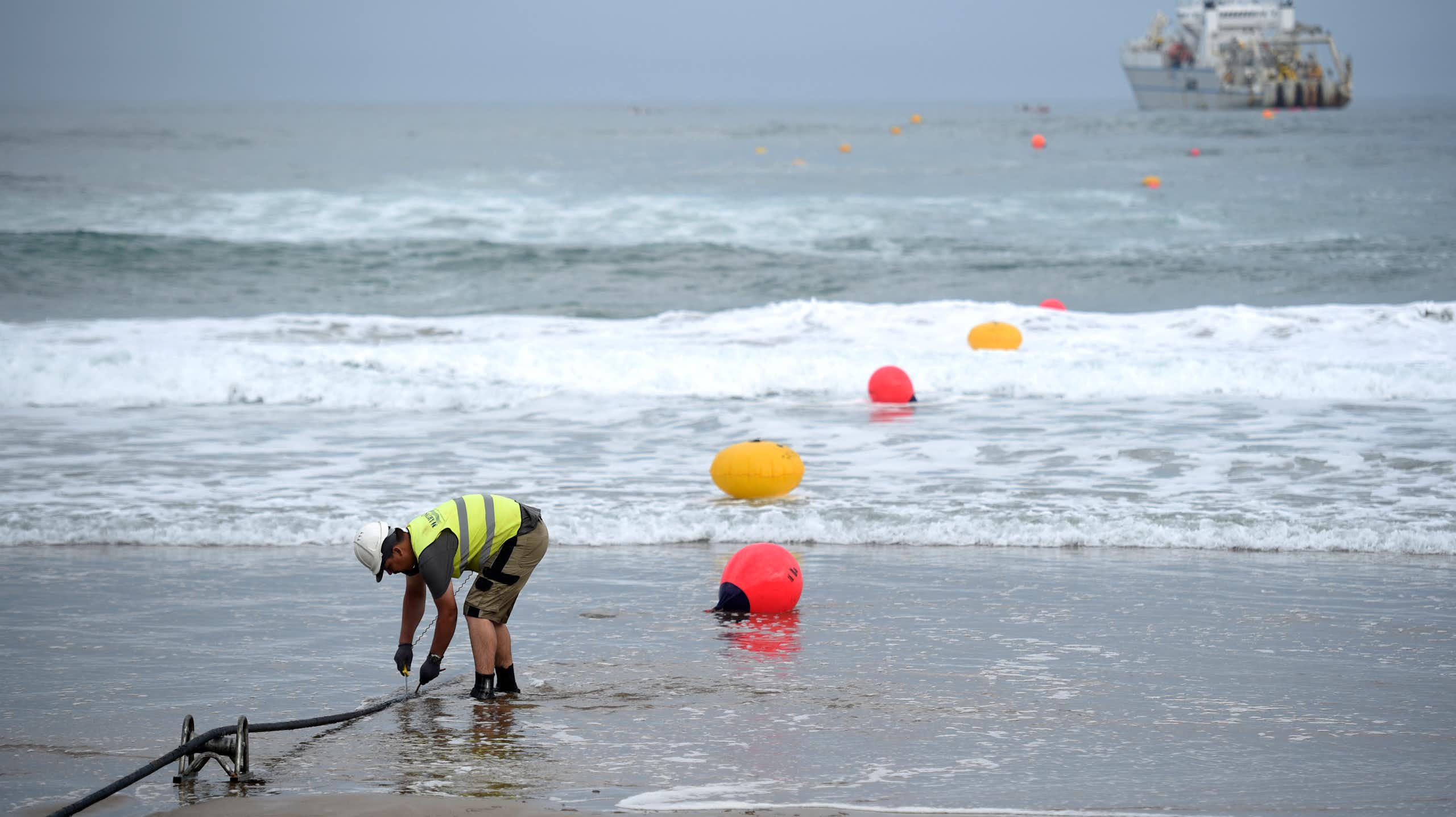 A man in a fluorescent vest works on a beach.