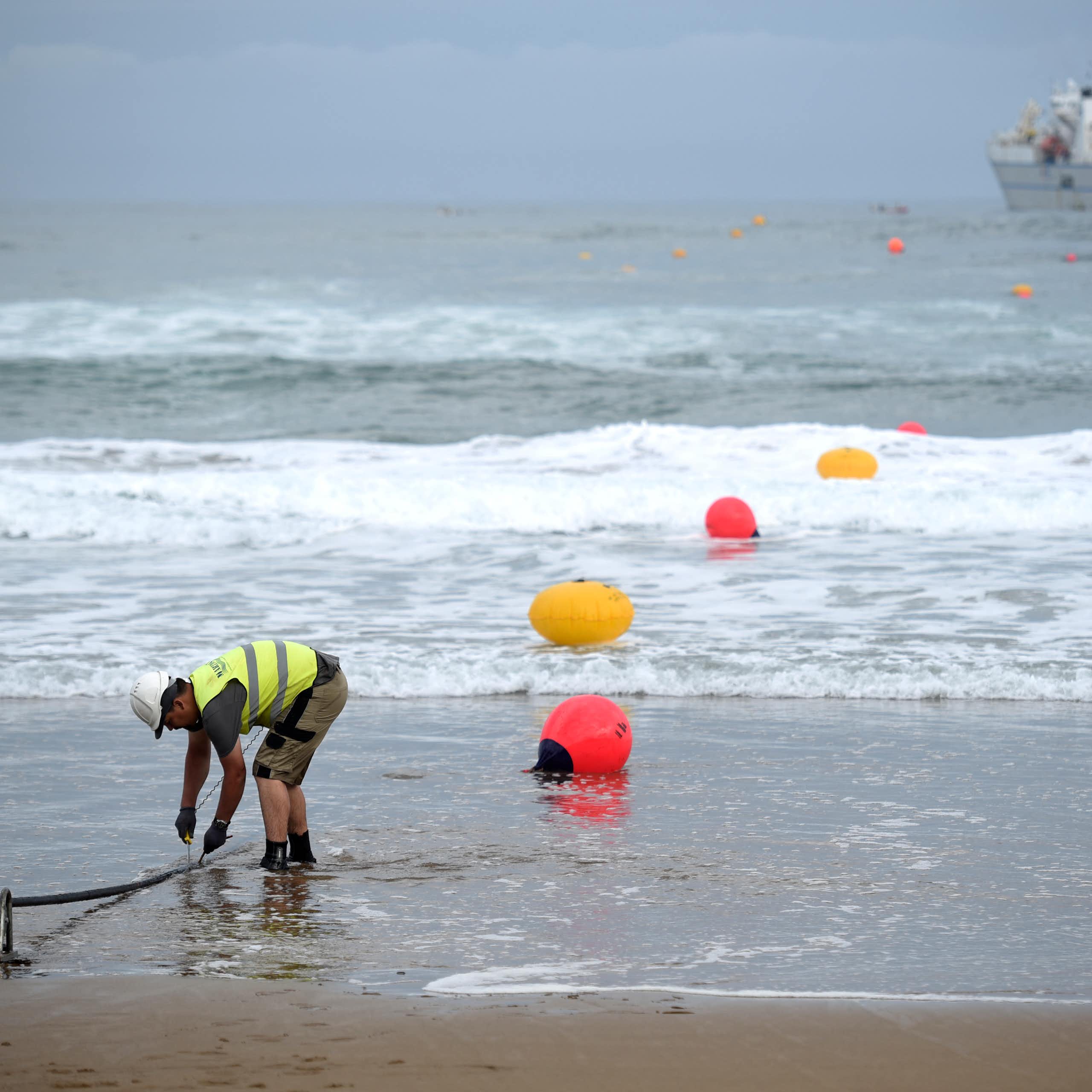 A man in a fluorescent vest works on a beach.