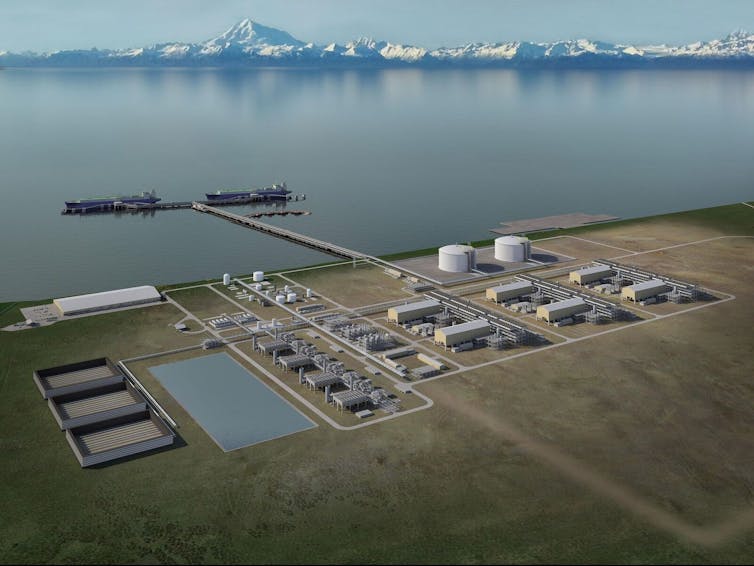 A group of large tanks and buildings, with a long pier out into the water where two cargo ships are tied up.