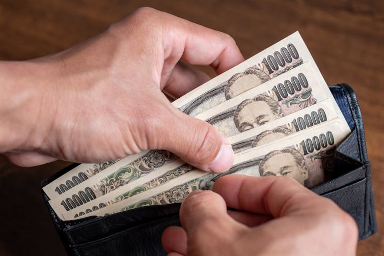 A man's hands taking Japanese banknotes from his wallet.