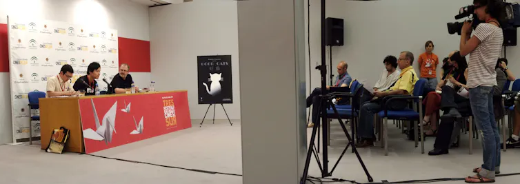 Imagen de una rueda de prensa en la que el cineasta está acompañado del presentador y de un intérprete.