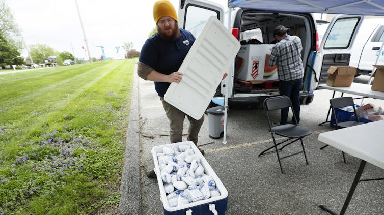 Man holds the lid of a large cooler filled with white plastic packages.