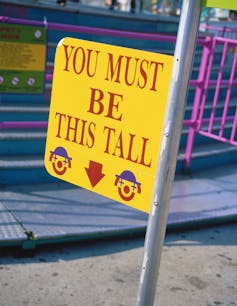 sign with two clown faces reads 'YOU MUST BE THIS TALL' with an arrow