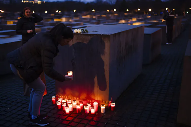 People seen hovering over candles at a large stone amid darkness.