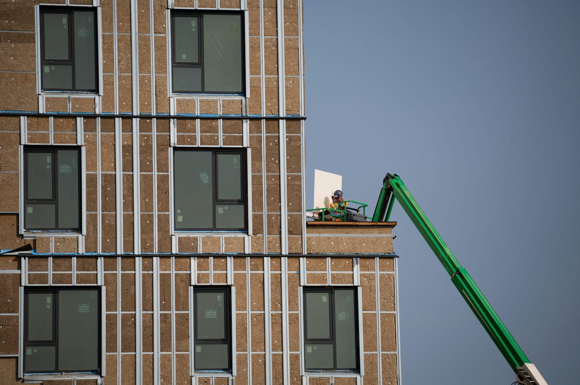 A construction worker uses an articulating boom lift on top of an apartment building