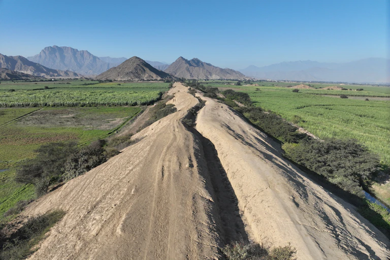 Um canal seco através de campos verdes com montanhas à distância