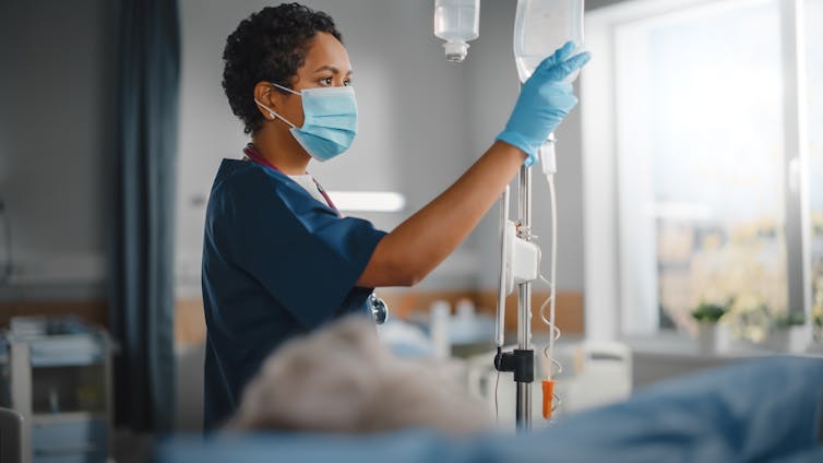 A nurse or doctor adjusts a drip in a hospital room.