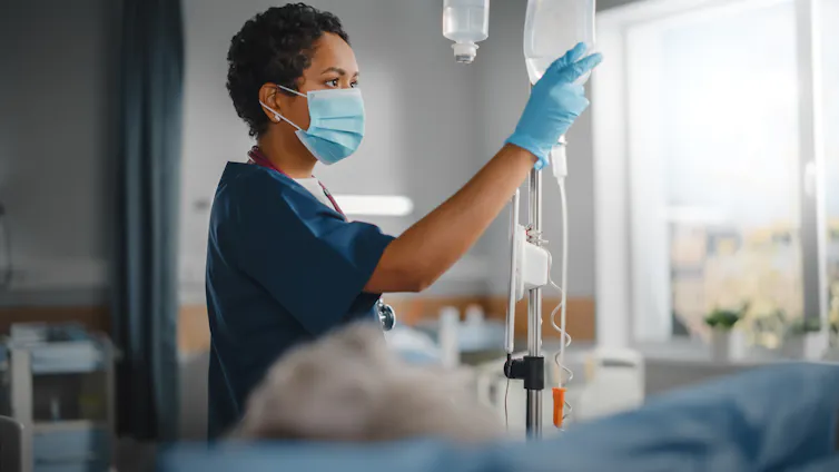 A nurse or doctor adjusts a drip in a hospital room.