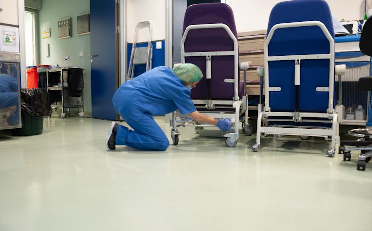 A woman on the ground cleaning hospital equipment.