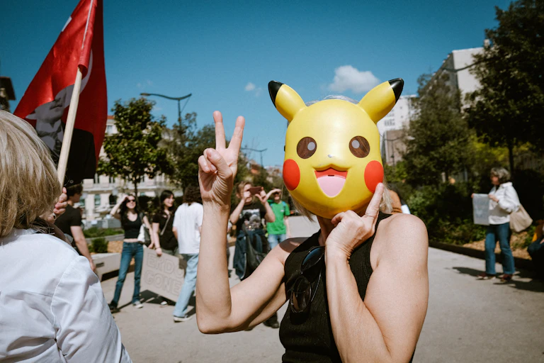A protester wearing a yellow mask of a cartoon character poses while making a peace symbol with their right hand.
