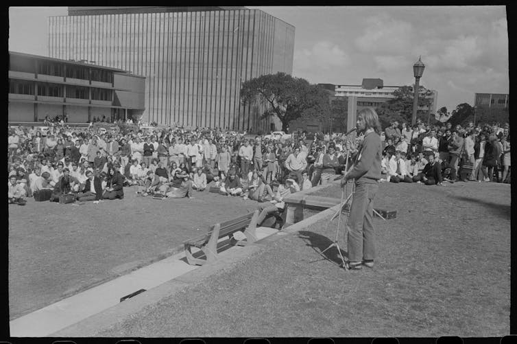 A man addresses a crowd of people on the lawns of Sydney University.