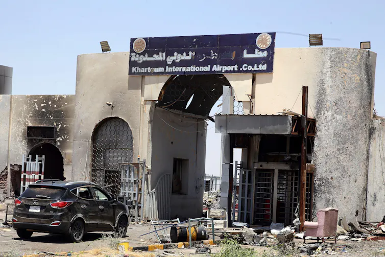 An undamaged car drives through the gates of Khartoum's airport, showing signs of heavy fighting and bombardment.