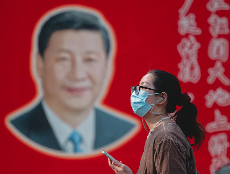 A woman walks in front of a portrait of Xi Jinping.