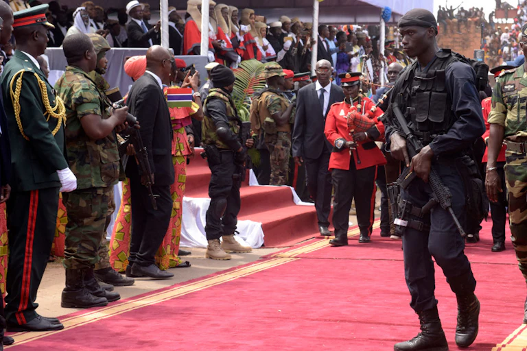 An armed soldier in combat gear clears the way for a red carpet ceremonial procession.
