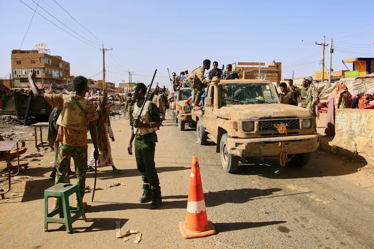 Trump tariff backflip brings a US industry warfare with China into the crosshairs 2 Armed troops from the Sudan Armed Forces in a convoy of pick-up trucks on a road beside which there is a small make-shift market.