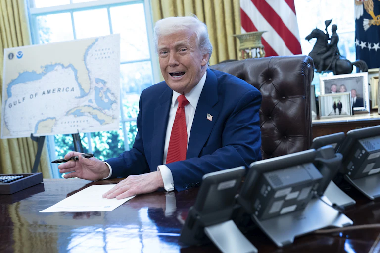 Donald Trump signs an executive order in the Oval Office in front of a map of the Gulf of America.