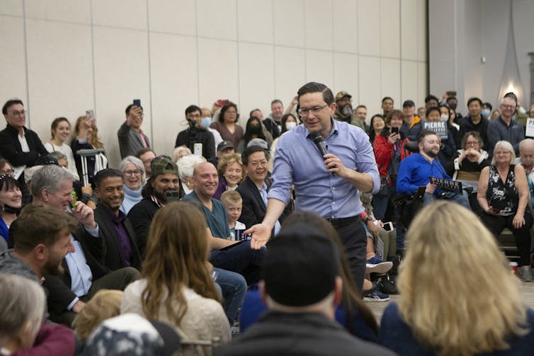 El hombre con las gafas se da la mano con una multitud sentada