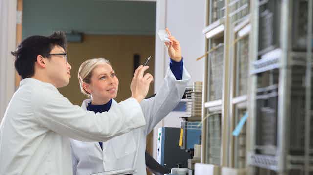 Two scientists look at a slide in a lab. One is pointing a finger at a result while another holds up the result.