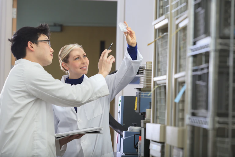 Two scientists look at a slide in a lab. One is pointing a finger at a result while another holds up the result.