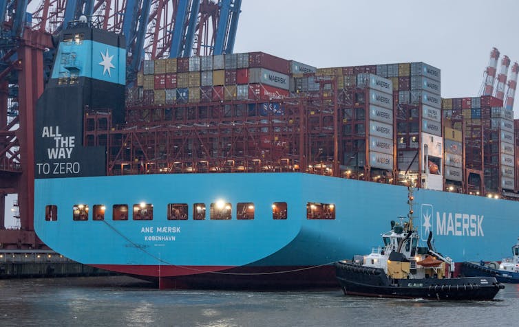A large carbon ship is at port being stacked with giant shipping containers.