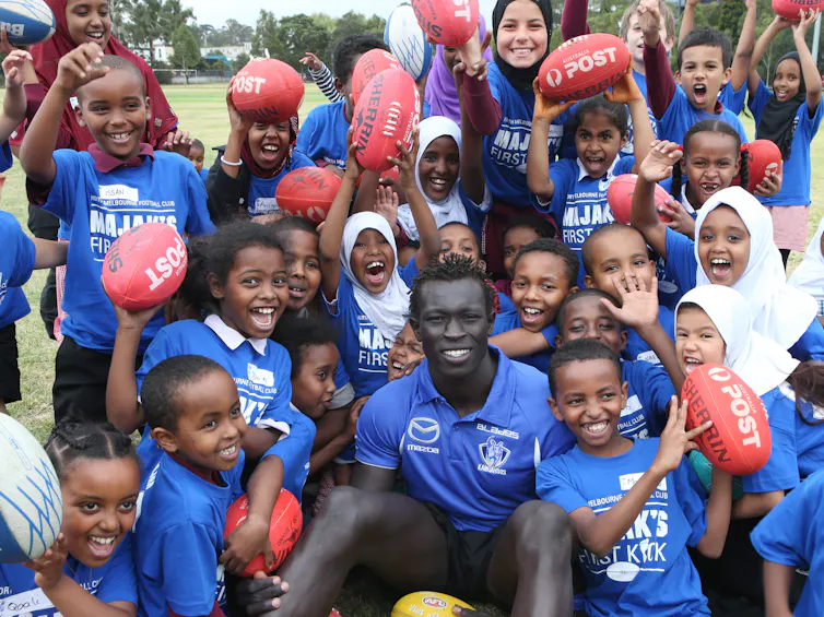 Dozens of happy children, some holding footballs, crowded around former AFL star Majak Daw
