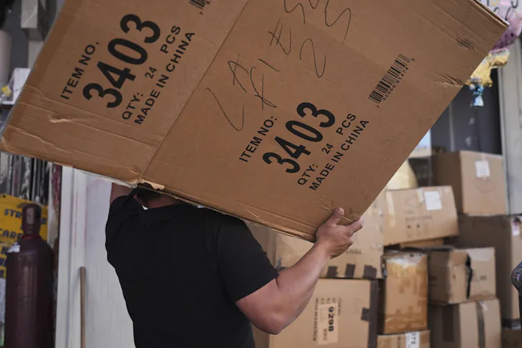 A person carries a cardboard box that says 'made in China' on it on their shoulder