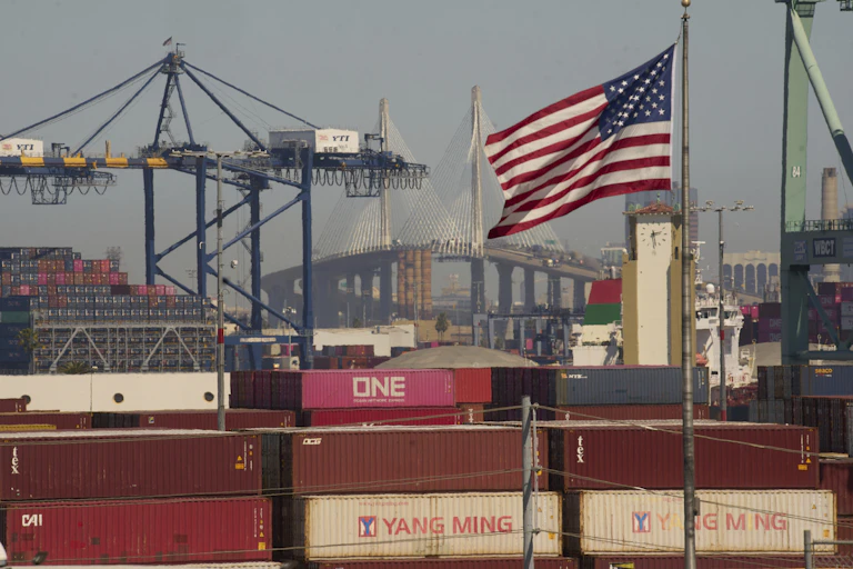 Shipping containers stacked at a port with an American flag seen in the foreground