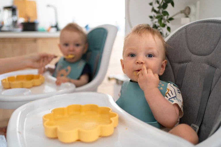 twin babies eating in high chairs