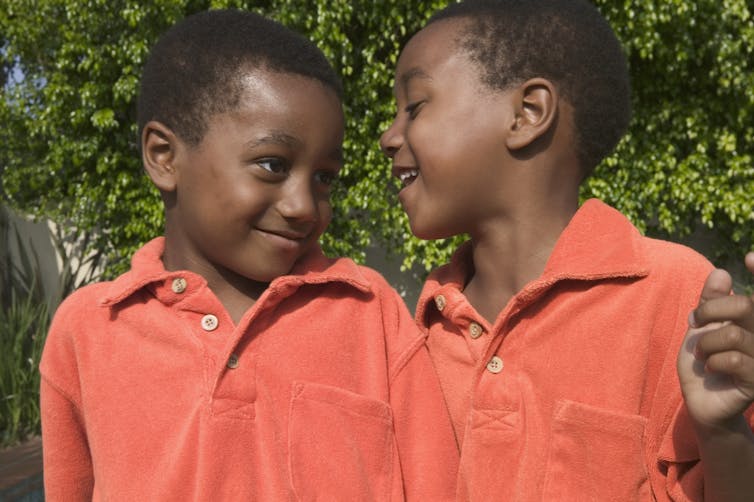 two boys in identical shirts side by side look at each other