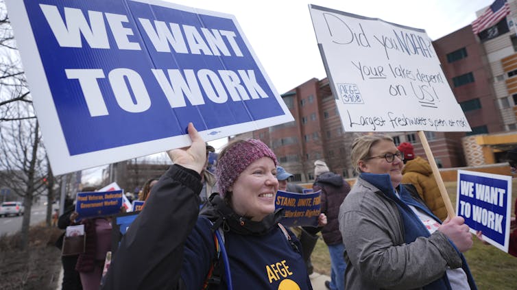 people at a protest, a woman holds a sign saying 'We Want to Work'