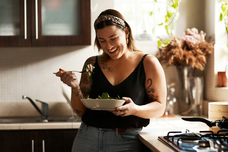 A woman eating a salad in a kitchen.